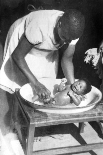 Een leerling-verpleegster wast een baby te Sumwe, Tanganjika (Tanzania)